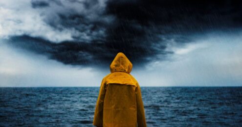 A man in a yellow coat staring at the Sea and a dark sky