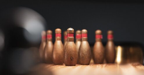 nonprofit blogs - Ten vintage bowling pens with a brown tent and red bands around the neck at the end of a lane and an out-of-focus bowling ball heading their way.