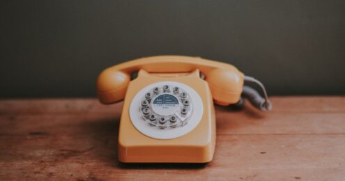 internal communications - orange rotary phone on wooden table and green wall background.