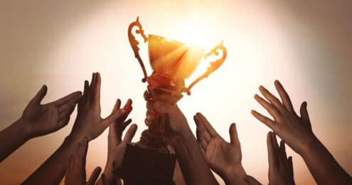 Post header image shows a bunch of hands raising up towards a trophy signifying that Executive Directors can crush your Annual Review in 10 Steps For Executive Directors