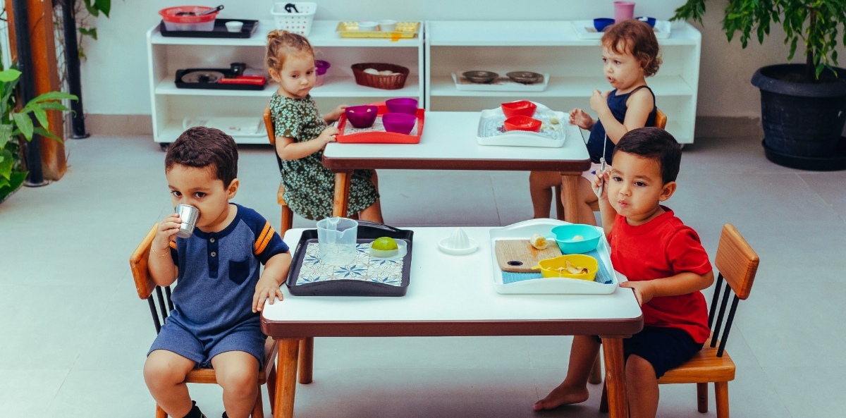 2 children sit at one table looking disappointingly at another table with two other children who seem unconcerned with the first two.