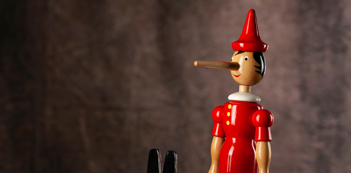 A wooden Pinocchio doll with an exaggeratedly long nose sits in front of a neutral backdrop, symbolizing the concept of lying or falsehood.