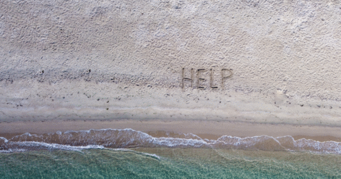 The words "help" appear in the sand on a beach.