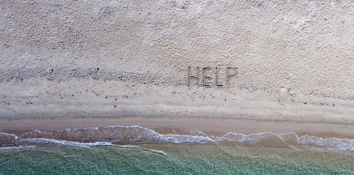 The words "help" appear in the sand on a beach.
