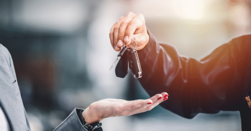 A person hands over car keys to another person, symbolizing the transfer of ownership.