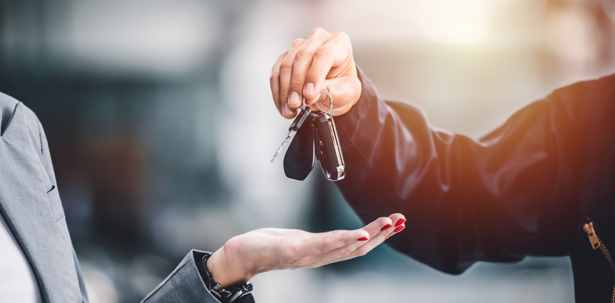 A person hands over car keys to another person, symbolizing the transfer of ownership.