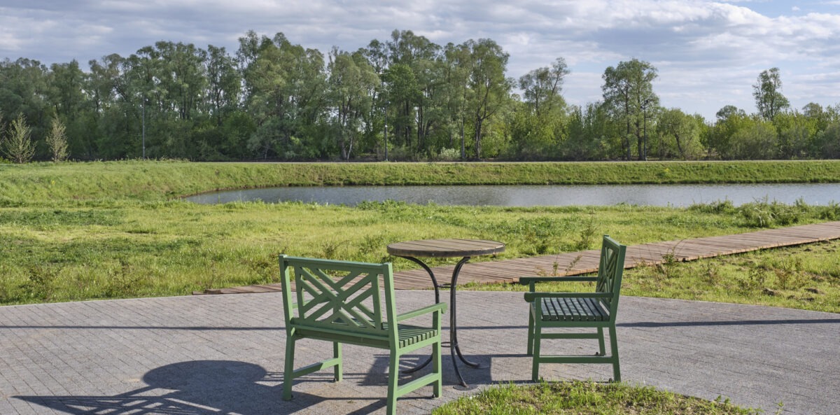 Two green chairs and a table overlooking a quiet pond, symbolizing conversation, connection, and hope in a divided world