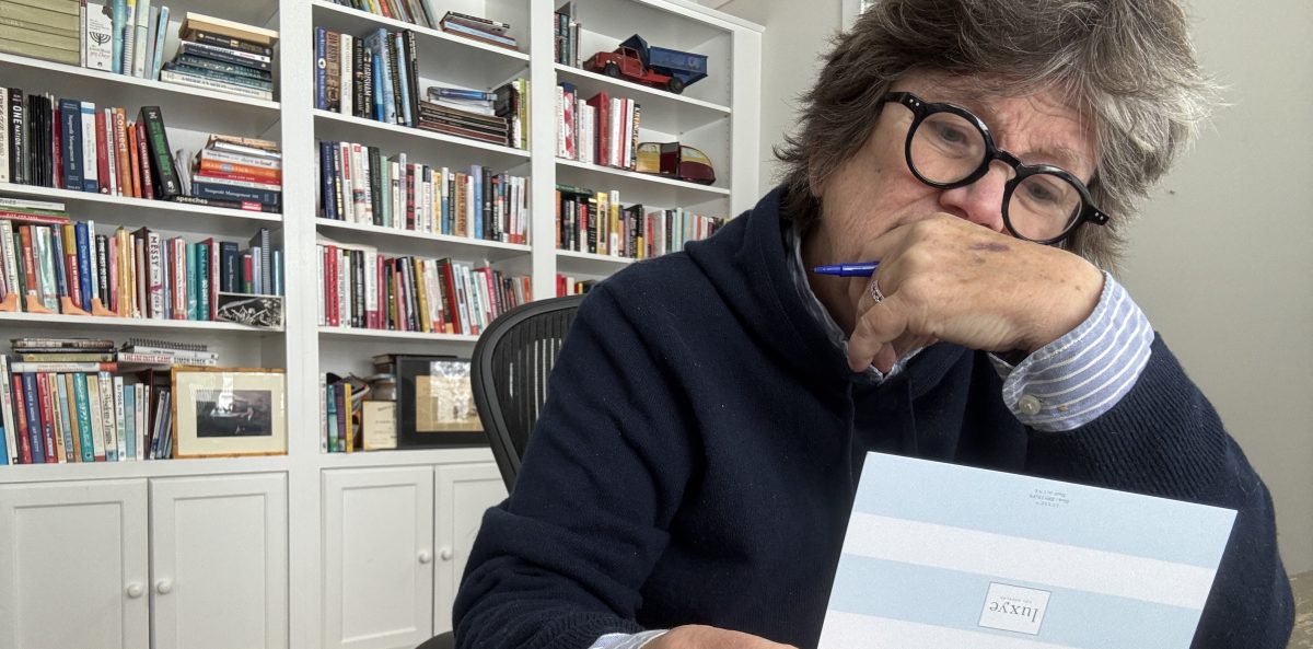 Joan Garry sits at her desk in a home office, holding a handwritten thank you appreciation note and pausing thoughtfully, with bookshelves behind her.