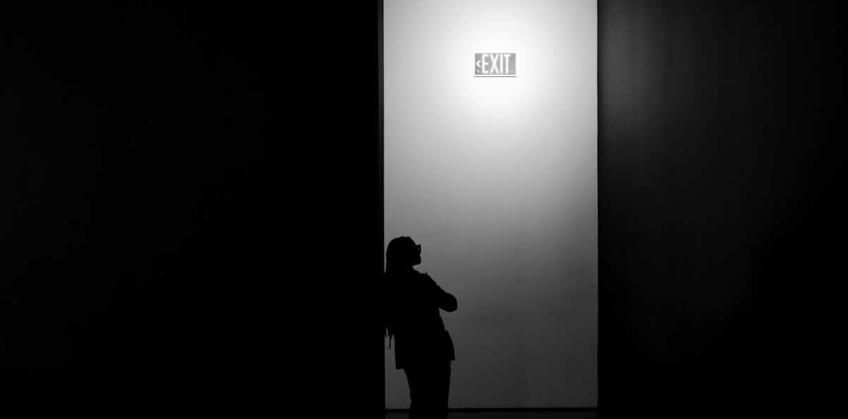 Silhouette of a person standing near a lit exit doorway, symbolizing leadership transition and the emotional complexity of letting go.